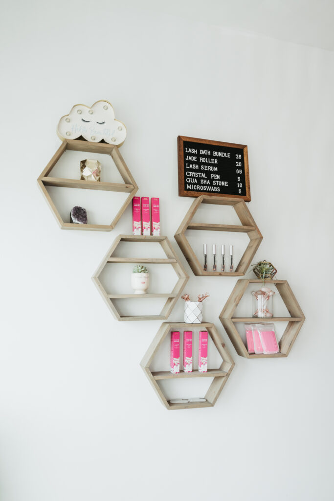 Hexagon shaped shelves on a wall in a beauty studio, holding pink boxes of eyelash and eye brow care products