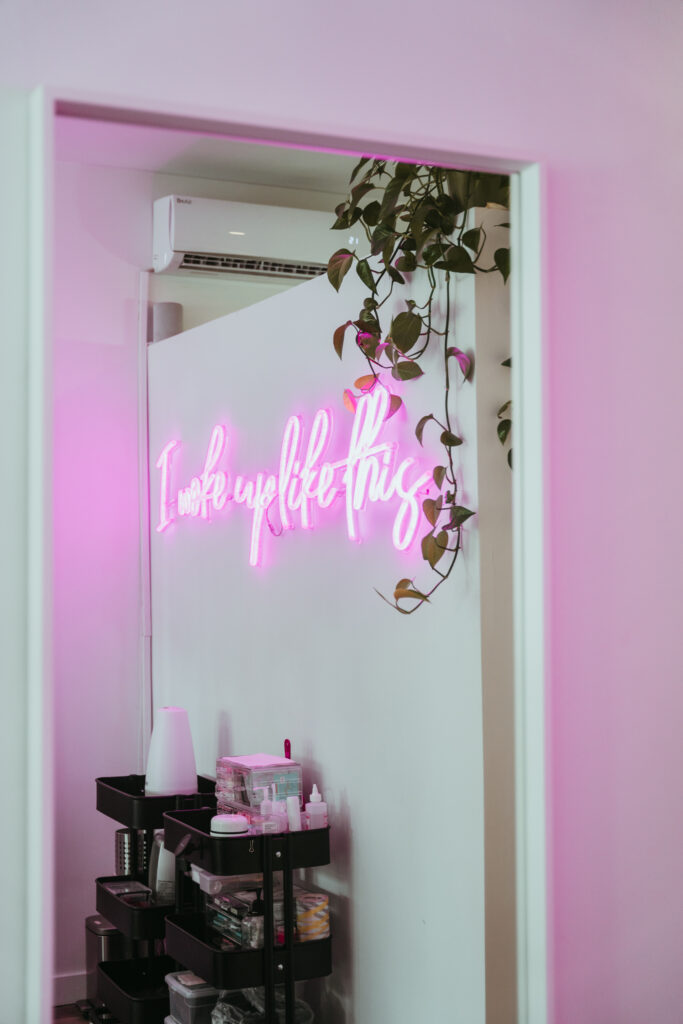 A mirror with a reflection of a pink neon sign that says "I woke up like this"