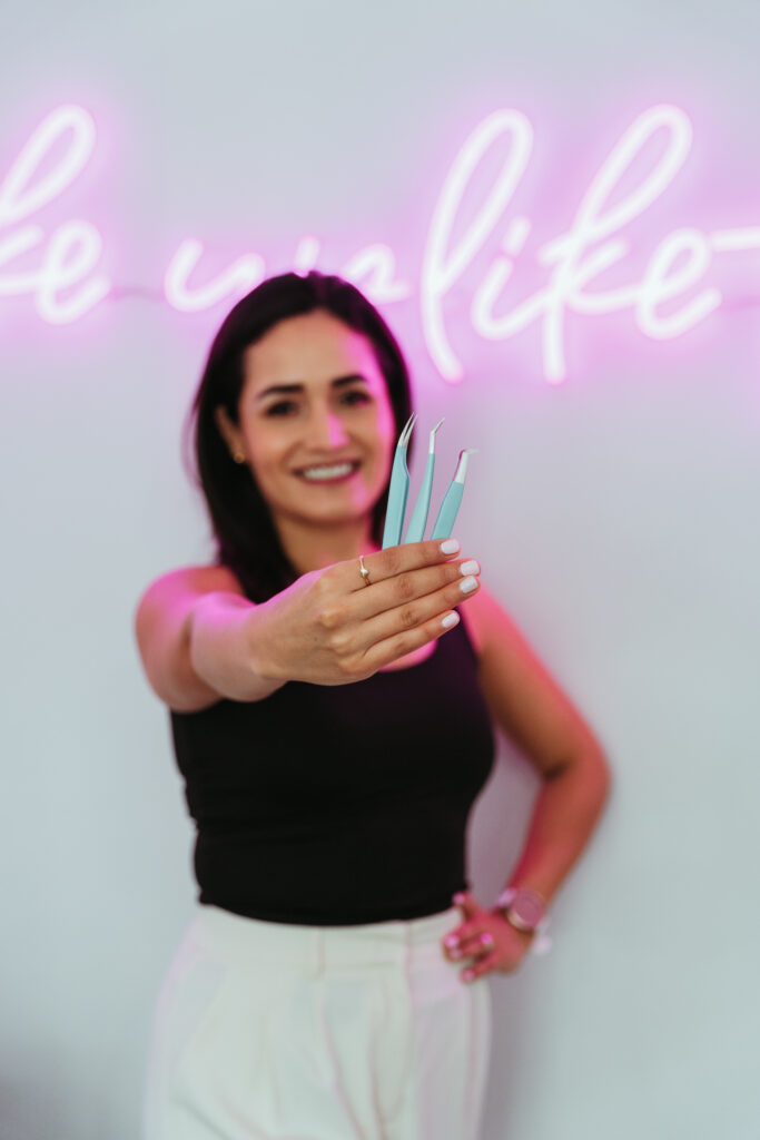 A woman holding 3 blue eyebrow tweezers in front of her face