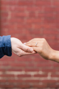 Focused detail on the woman’s hand with her engagement ring resting in her partner’s.