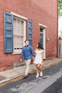 The couple strolls down a quiet alleyway, sharing smiles as they hold hands beside charming historic architecture.