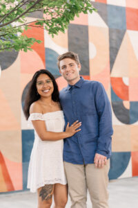 The couple stands in front of a bold geometric mural, sharing a happy moment.