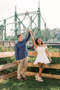 A whimsical photo of the couple twirling near a riverside bridge.