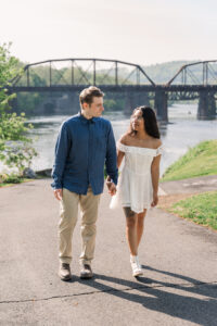 The couple enjoys a stroll along a paved riverside path with scenic views in the background.