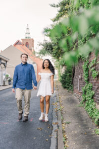 The couple smiles as they walk side by side along a quiet street lined with greenery and charm.