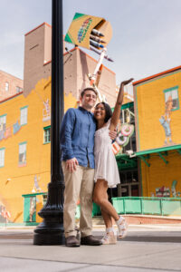 The couple poses under a retro Crayola sign with bright colors, bringing a fun pop to their gallery.