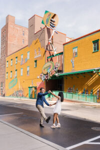 A joyful and spontaneous moment of the couple dancing on the street in front of the bright yellow Crayola Experience building in Easton, Pennsylvania.