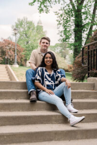 Relaxed and happy, the couple sits side by side on the stairs of a campus-like setting.