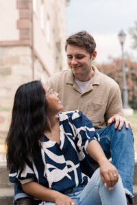 The couple sits close together, exchanging loving glances on the steps of a historic building.