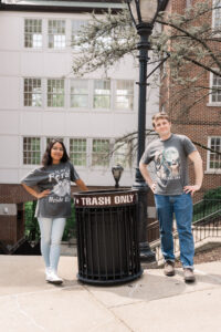 Two people stand on either side of a trash can labeled "TRASH ONLY," posing with playful confidence. They wear matching t-shirts that say "in my feral era" and "Bride Era."
