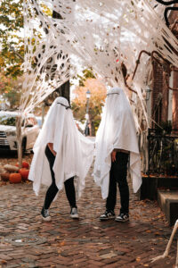 A ghost-costumed couple holds hands beneath a white canopy of gauze and fall decorations.