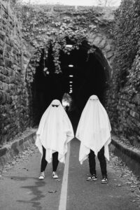 A couple dressed as ghosts walks down a shadowy stone tunnel toward the camera.